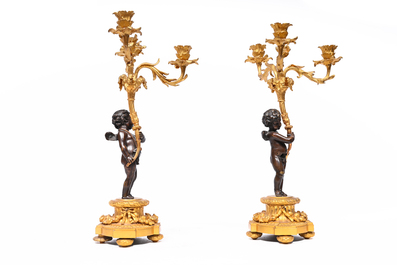 A pair of French patinated and gilt bronze three-light candlesticks in the form of a putto carrying a bouquet of flowers, 19th C.