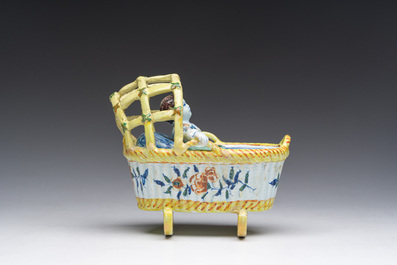 A polychrome Dutch Delft model of a cradle with child, 19th C.