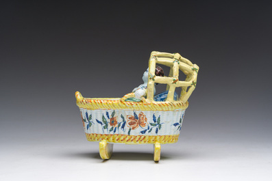 A polychrome Dutch Delft model of a cradle with child, 19th C.