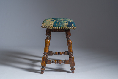 A wooden stool with turned legs upholstered with a fragment of a Flemish wall tapestry, 17th C.