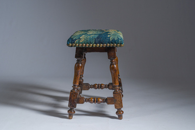 A wooden stool with turned legs upholstered with a fragment of a Flemish wall tapestry, 17th C.