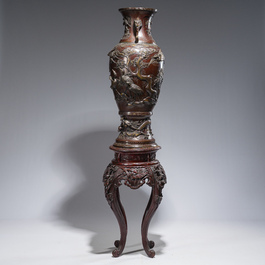A large Japanese bronze vase with relief design of cranes, dragons and birds on a wooden stand with floral design, Meiji, 19th/20th C.