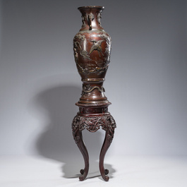 A large Japanese bronze vase with relief design of cranes, dragons and birds on a wooden stand with floral design, Meiji, 19th/20th C.