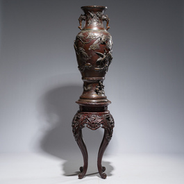 A large Japanese bronze vase with relief design of cranes, dragons and birds on a wooden stand with floral design, Meiji, 19th/20th C.