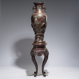 A large Japanese bronze vase with relief design of cranes, dragons and birds on a wooden stand with floral design, Meiji, 19th/20th C.