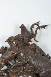 A large carved wooden 'Black Forest' clock with a deer hunt on a console tabel with floral design, 19th/20th C.