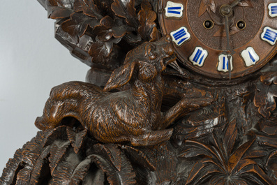 A large carved wooden 'Black Forest' clock with a deer hunt on a console tabel with floral design, 19th/20th C.