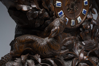 A large carved wooden 'Black Forest' clock with a deer hunt on a console tabel with floral design, 19th/20th C.