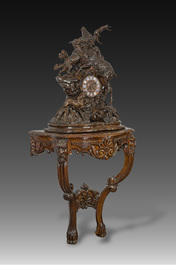 A large carved wooden 'Black Forest' clock with a deer hunt on a console tabel with floral design, 19th/20th C.
