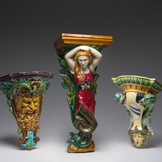 Three French polychrome maiolica consoles with a siren, a mascaron and a coat of arms, one with a Sarreguemines mark, early 20th C.