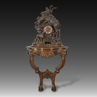 A large carved wooden 'Black Forest' clock with a deer hunt on a console tabel with floral design, 19th/20th C.