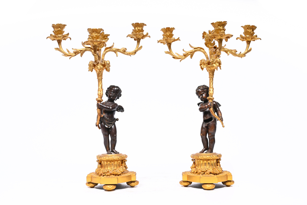 A pair of French patinated and gilt bronze three-light candlesticks in the form of a putto carrying a bouquet of flowers, 19th C.