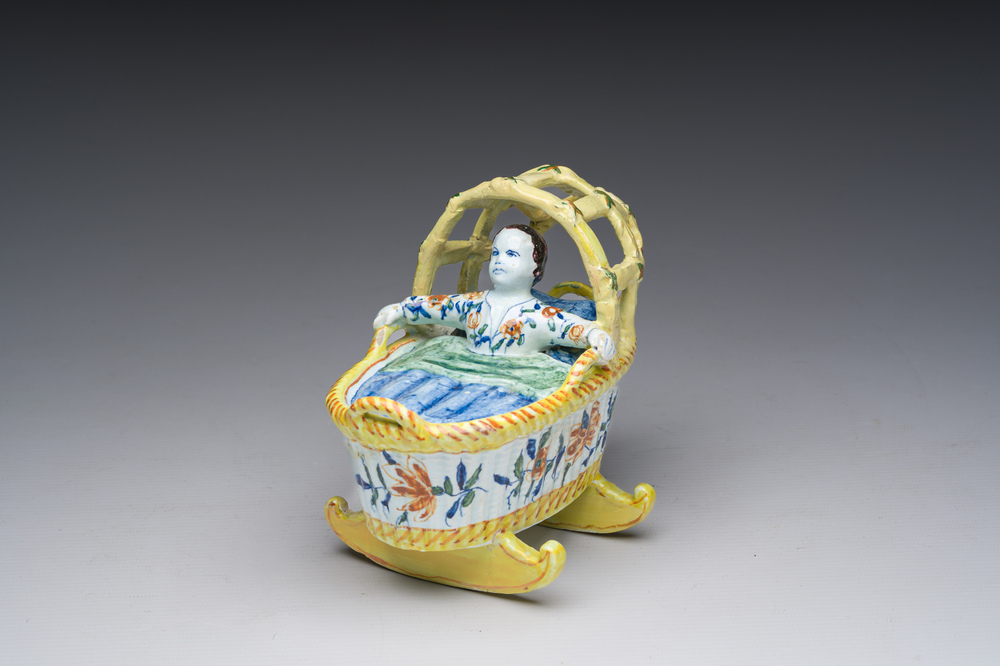 A polychrome Dutch Delft model of a cradle with child, 19th C.