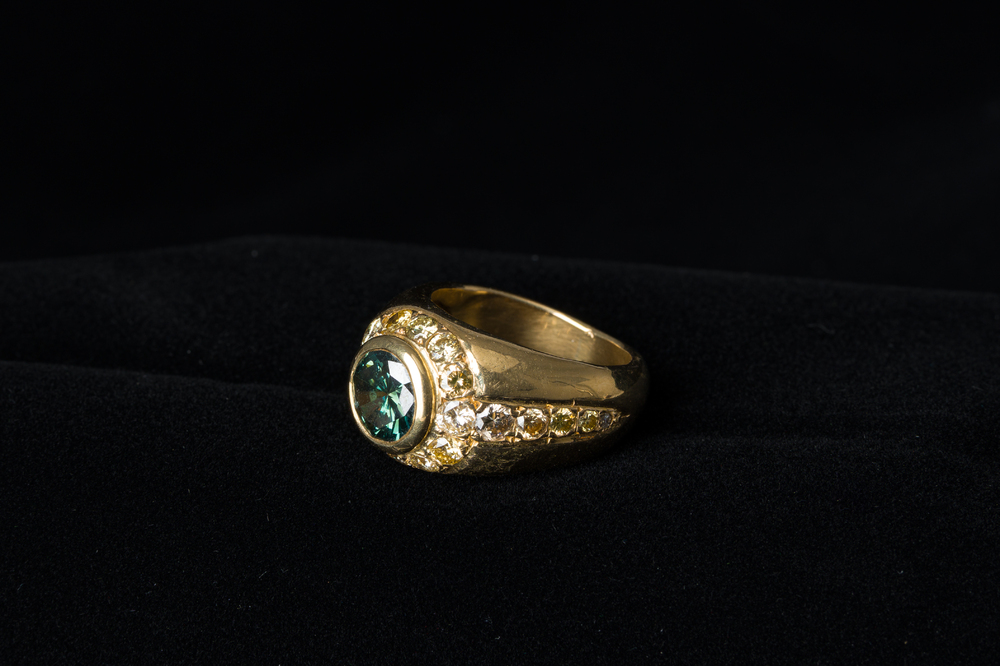 An 18 carat yellow gold men's ring with a central green-blue diamand of 1,98 carats and finished with various other diamonds, 20th C.