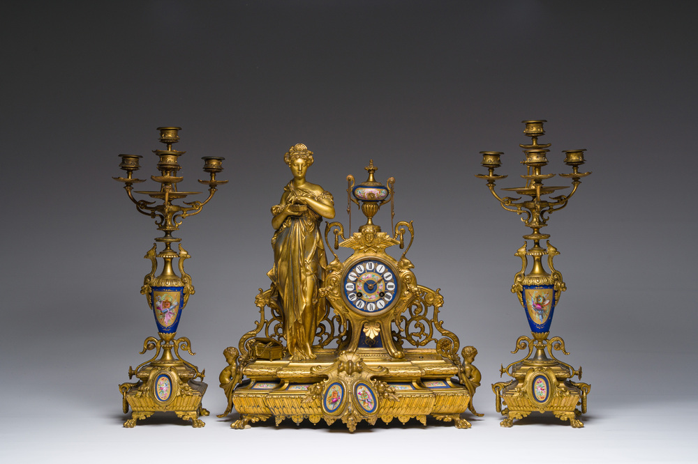 Een Franse driedelige schouwgarnituur in verguld kunstbrons bekroond met een dame met een juwelenkoffer in de hand, 19de eeuw