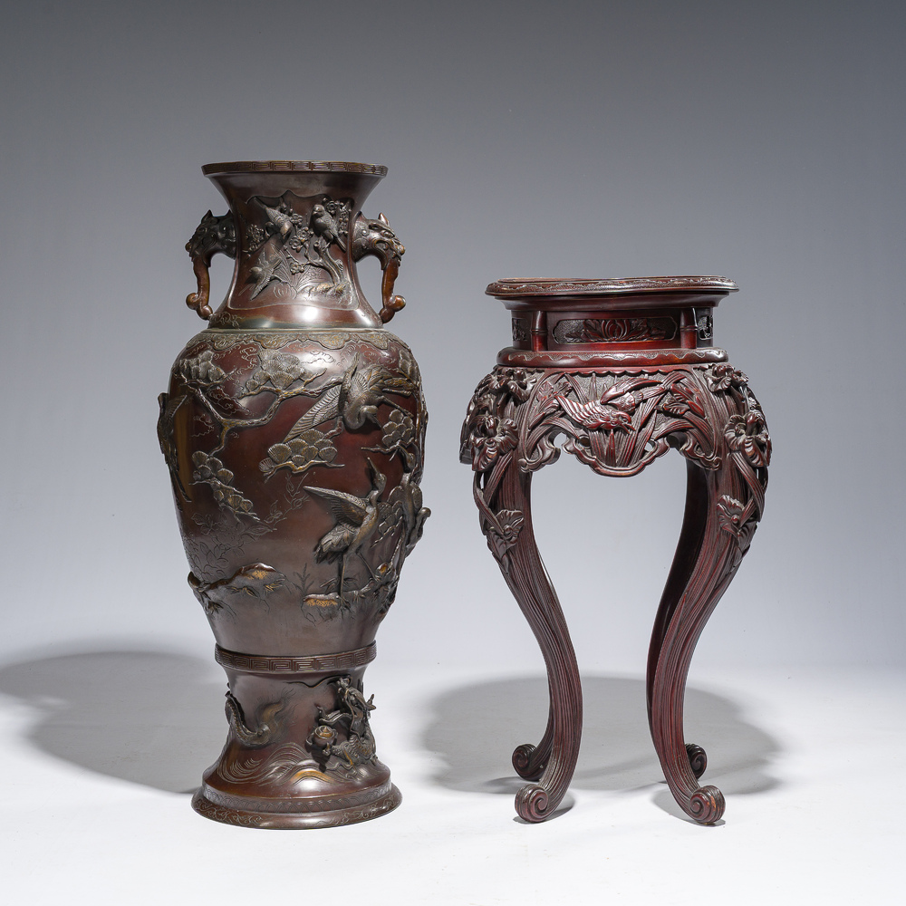 A large Japanese bronze vase with relief design of cranes, dragons and birds on a wooden stand with floral design, Meiji, 19th/20th C.
