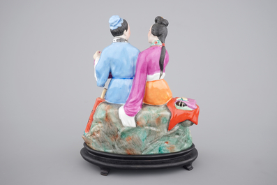 A Chinese porcelain model of an amorous couple, on wooden stand, 20th C.