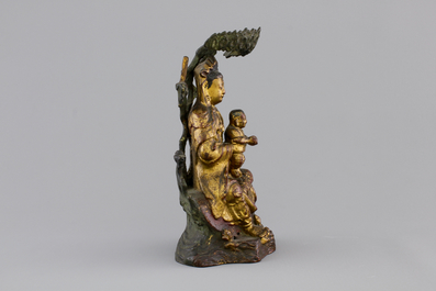 A Chinese bronze and gilt Buddha with child, seated beneath a bodhi tree, 17/18th C.