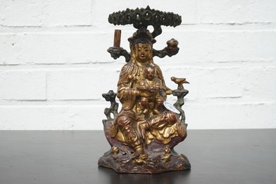 A Chinese bronze and gilt Buddha with child, seated beneath a bodhi tree, 17/18th C.