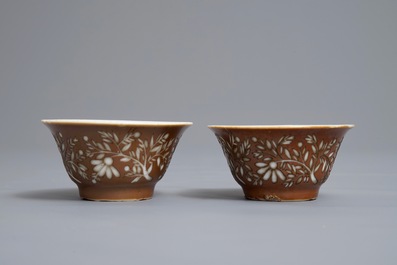 Une paire de tasses et soucoupes en porcelaine de Chine bleu et blanc &agrave; d&eacute;cor grav&eacute; sur fond brun capucin, Kangxi