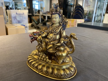 A Tibetan gilt bronze group of Jambhala on his lion, 19/20th C.