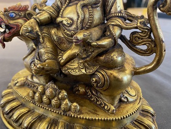 A Tibetan gilt bronze group of Jambhala on his lion, 19/20th C.