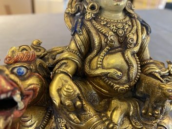 A Tibetan gilt bronze group of Jambhala on his lion, 19/20th C.