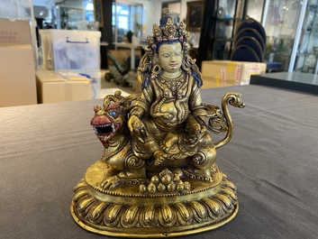 A Tibetan gilt bronze group of Jambhala on his lion, 19/20th C.