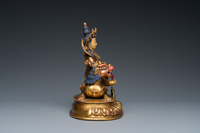 A Tibetan gilt bronze group of Jambhala on his lion, 19/20th C.