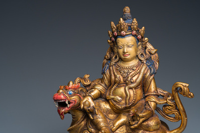 A Tibetan gilt bronze group of Jambhala on his lion, 19/20th C.