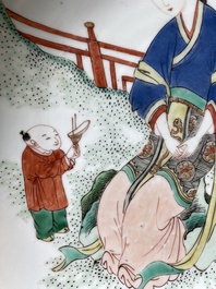 A Chinese famille verte dish with a lady in a garden and a boy offering her a 'jue' vessel, Kangxi