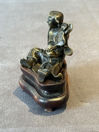 A Chinese bronze paperweight in the form of 'Shi De 拾得' on wooden stand, 16th C.