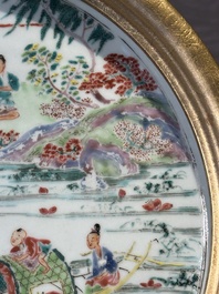 A Chinese famille rose plate with figures in a river landscape in gilt wooden frame, Yongzheng