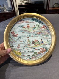 A Chinese famille rose plate with figures in a river landscape in gilt wooden frame, Yongzheng
