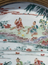 A Chinese famille rose plate with figures in a river landscape in gilt wooden frame, Yongzheng