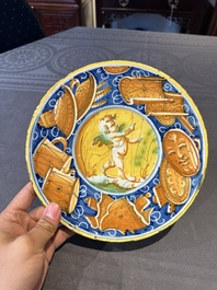 A polychrome Italian maiolica plate with a putto surrounded by trophies, Pesaro, 16th C.