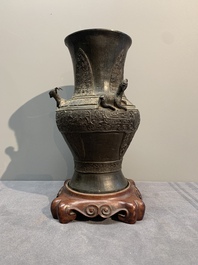 A Chinese archaistic bronze 'gu' vase and a 'hu' vase with rams in relief on a wooden stand, 18/19th C.