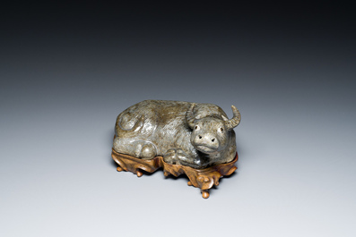 A Chinese brown-grey-glazed recumbent water buffalo on wooden stand, 19th C.