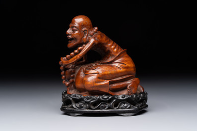 A Chinese fine huanghuali sculpture of a Luohan on a zitan stand, Qianlong mark, 19/20th C.