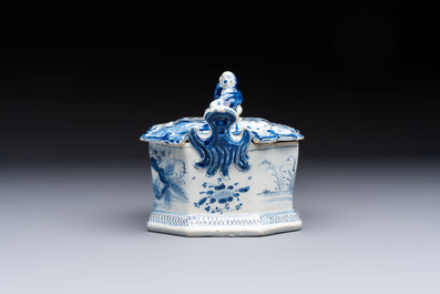 A blue and white Dutch Delft chinoiserie butter tub with a reclining figure finial, 18th C.