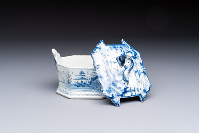 A blue and white Dutch Delft chinoiserie butter tub with a reclining figure finial, 18th C.