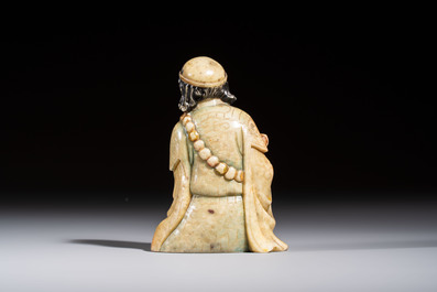 A Chinese gilt-polychromed soapstone Luohan on a wooden stand, 19th C.
