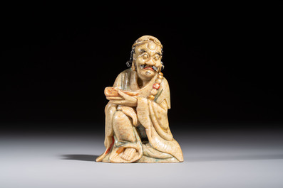 A Chinese gilt-polychromed soapstone Luohan on a wooden stand, 19th C.