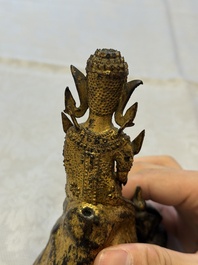 A Thai gilt-bronze figure of a seated deity with attendant animals, 19th C.