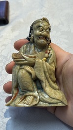 A Chinese gilt-polychromed soapstone Luohan on a wooden stand, 19th C.