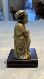 A Chinese gilt-polychromed soapstone Luohan on a wooden stand, 19th C.