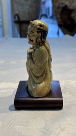 A Chinese gilt-polychromed soapstone Luohan on a wooden stand, 19th C.