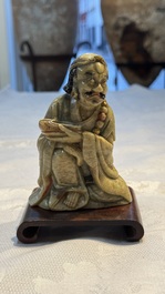 A Chinese gilt-polychromed soapstone Luohan on a wooden stand, 19th C.