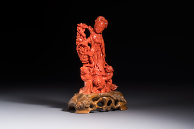 A Chinese carved red coral 'Goddess and Boys' group on a wooden stand, 19/20th C.