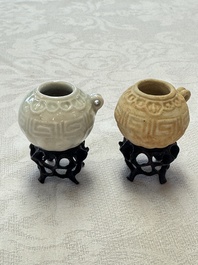A pair of Chinese bird feeders with moulded design, one unglazed, on later wooden stands, Song
